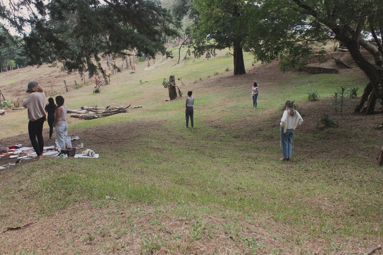 Un prado verde rodeado de árboles, con algunas personas de pie a lo lejos.